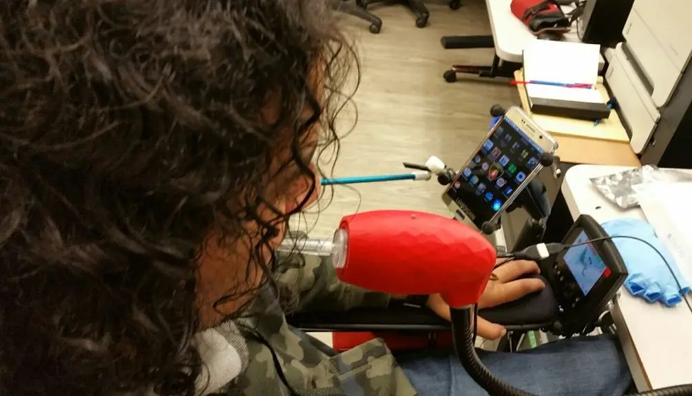 An individual using their breath to interact with a smartphone through a sip-and-puff device