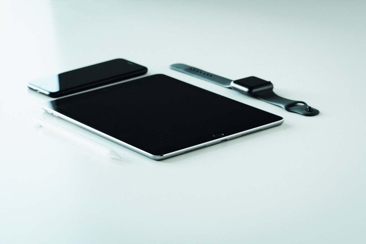 A collection of digital devices laid out on a table including a smartwatch, phone and tablet